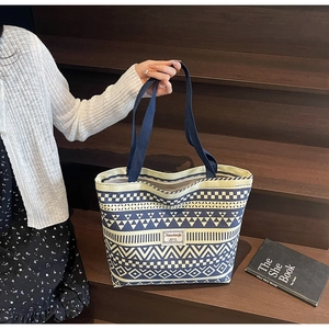 Close-up of geometric pattern canvas tote bag with blue weave handles and brand label