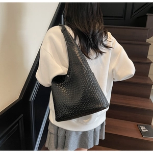 Close-up of black woven texture hobo bag worn over the shoulder in a minimalist setting