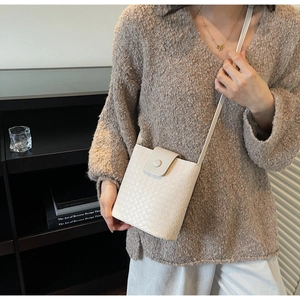 Detail of cream woven cross-pattern texture and flap closure on a bucket crossbody bag