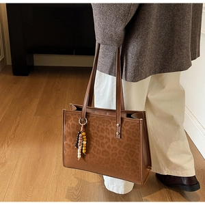 Detail of large leopard print tote bag featuring beaded charm and premium leather trim