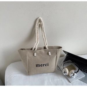 Detail of beige linen tote bag with rope handles and merci print on minimalist desk