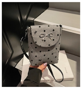 Detail of grey felt crossbody bag featuring black polka dots and silver metal bow clasp