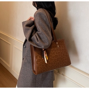 Detail of leopard print tote bag with brown leather straps and beaded tassel charm