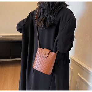 Detail of woven brown leather crossbody bag paired with elegant black coat outfit