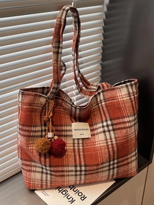 Large capacity orange plaid tote bag with fur ball charm leaning on white blinds