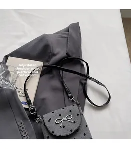 Detail of grey polka dot crossbody bag featuring a silver bow and adjustable strap