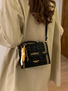 Leopard print crossbody bag with gold studs and wooden bead charm on khaki trench coat
