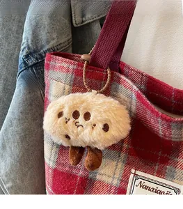 Detail view of a beige plush doll charm with embroidery on a red checkered tote bag