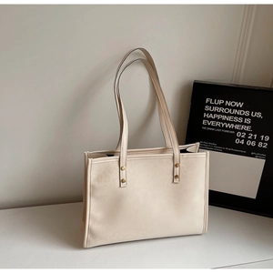 Detail of cream tote bag with minimalist PU leather texture and gold metal rivet accents