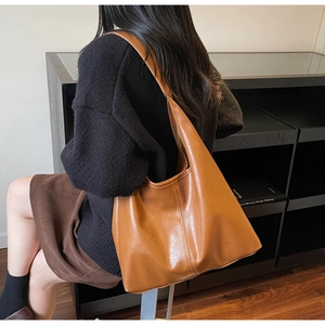 Brown faux leather tote bag with pebble texture and wide shoulder strap in daily use