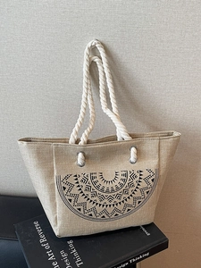 Beige linen tote bag with black tribal pattern and white rope handles on a book
