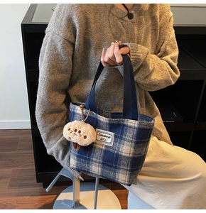 Detail of blue plaid tote bag with plush mushroom charm and brand tag on textured fabric