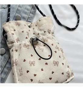 Detail of beige corduroy phone bag with heart prints and adjustable woven shoulder strap