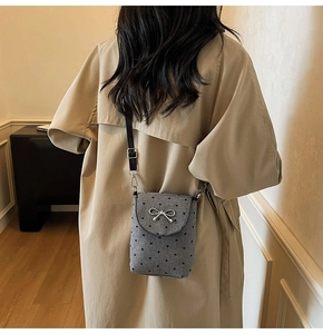Detail of grey crossbody phone bag with heart patterns and silver bow on beige coat