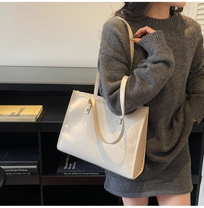 Detail of cream leather tote bag with metal studs worn with a grey knit dress