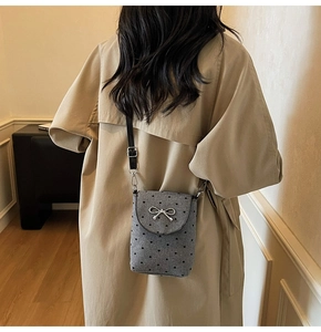 Detail showing the gray crossbody bag with heart patterns and silver bow on model back