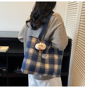 Detail of blue plaid tote bag with wide strap and plush pendant on model
