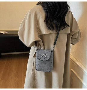 Detail of gray tweed mini crossbody bag with heart pattern and silver bow on trench coat