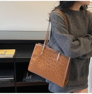 Detail of leopard print tote bag with brown leather trim and metal rivet reinforcement