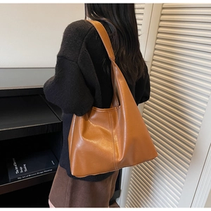 Shoulder view of a large caramel tote bag showing the drape and wide strap on a model