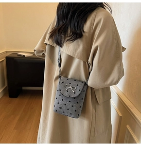 Detailed view of grey polka dot crossbody phone bag with metal bow on khaki trench coat