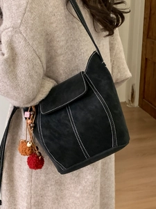 Black faux suede bucket bag with contrast stitching and colorful pom-pom charms