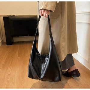 Detailed view of a minimalist black hobo tote bag styled with a beige trench coat