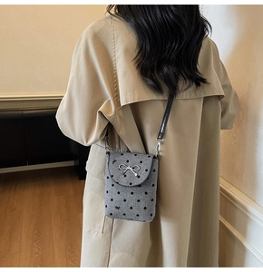 Close-up of a grey polka dot crossbody bag with a silver bow and leather strap