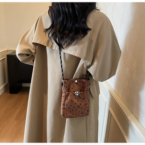 Detailed view of brown corduroy phone bag with black heart patterns and bow decor