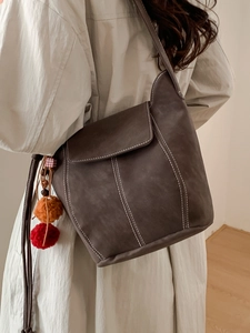 Deep brown minimalist bucket bag with white stitching and decorative pom-pom pendant