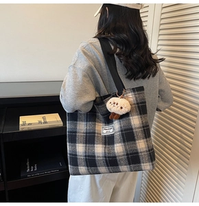 Detail of checkered canvas tote bag with shoulder strap and plush doll pendant