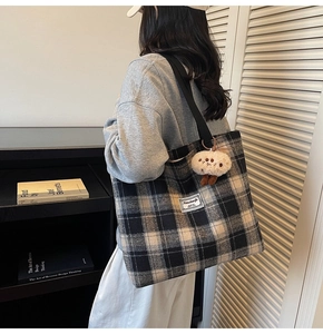 Detail of checkered wool tote bag with black strap and plush charm on a female model