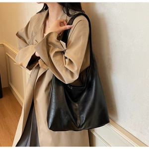 Minimalist black leather hobo tote bag shown worn with a beige trench coat for workwear