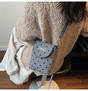 Detail of grey polka dot crossbody bag with a silver bow on a knitted sweater