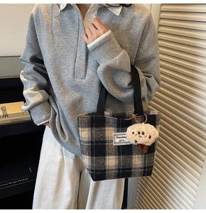 Detail of checkered tote bag with woven handles and cute plush charm on a grey sweatshirt