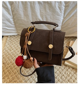 Dettaglio borsa a tracolla vintage marrone scuro con ciondolo su sfondo intrecciato
