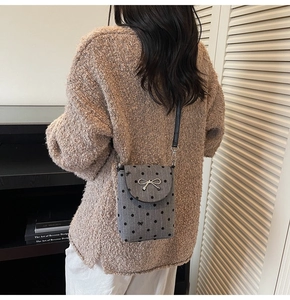Detail shot of a grey polka dot crossbody bag with a silver metal bow on a model