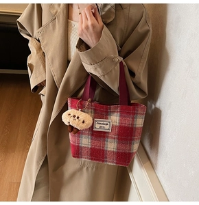 Detail of red plaid tote bag with plush mushroom charm on khaki trench coat