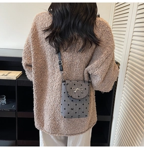 Detail of grey polka dot crossbody bag with silver bow ornament on knit sweater
