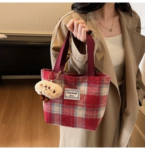 Detail of red checkered tote bag featuring a plush charm and woven shoulder strap