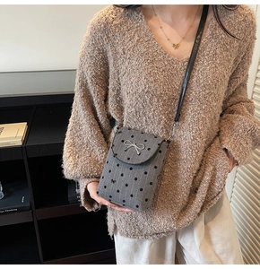 Close-up of grey polka dot crossbody bag with silver metal bow and black leather strap