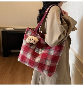 Detail of red checkered tote bag featuring a cute plush mushroom charm and shoulder strap