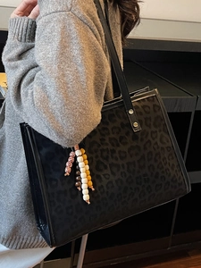 Large capacity black leopard print tote bag with beaded tassel charm on woman shoulder