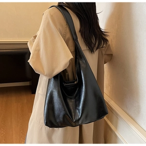 Detail of minimalist black leather tote bag with wide strap worn over a beige trench coat