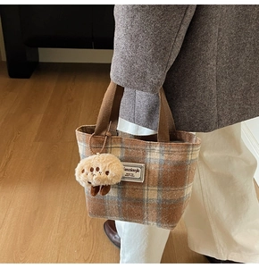 Detail of plaid wool tote bag with soft plush charm and sturdy brown handles