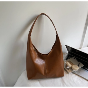 Close-up of caramel brown tote bag with stitching detail beside lifestyle props