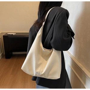 Hobo style cream tote bag with leather texture shown on shoulder of model in suit