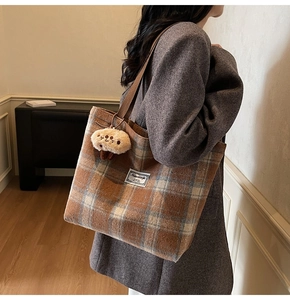 Close-up of brown plaid tote bag with plush mushroom charm and white fabric label detail