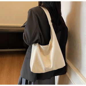 Detailed side view of a large cream hobo tote bag worn by a model in a cozy indoor setting