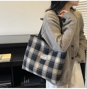 Close-up of black and white checkered tote bag with woven label shown on person in a library